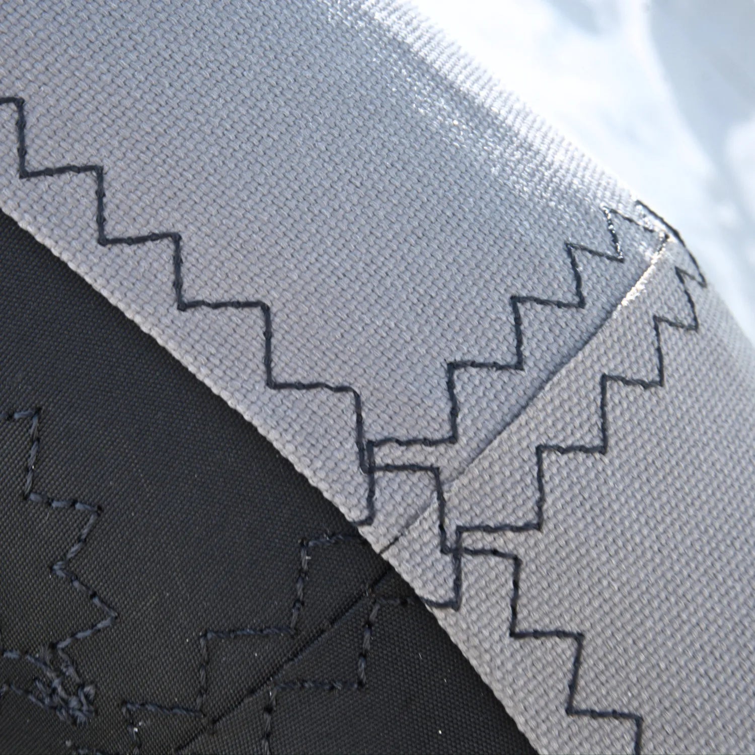 Close-up of the radius-curve on the AeroCasing™ perimeter showing black industrial zigzag stitching on the gray Mach-Shield 45™ technical fabric.