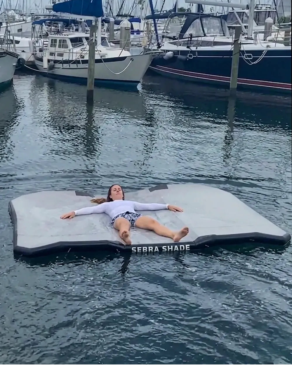 A woman relaxing on the Sebba Shade inflatable float at a marina party.